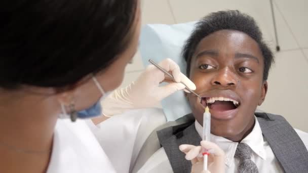 Legt der Zahnarzt einen Schuss eingefrorenes Novocain in den Kiefer. junger afrikanisch-amerikanischer Patient auf dem Stuhl in der Zahnklinik. Medizin, Gesundheit, Stomatologie-Konzept. — Stockvideo