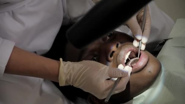 Tandläkaren behandlar patienten genom ett mikroskop. Ung African American manlig patient på stolen vid tandvårdsklinik. Medicin, hälsa, Stomatologi koncept. — Stockvideo