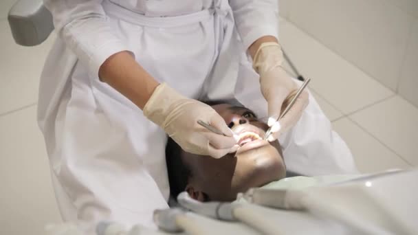 Une femme médecin dentiste utilise un microscope. Jeune homme afro-américain à la clinique dentaire. Médecine, santé, stomatologie concept. dentiste effectue l'inspection et conclut . — Video