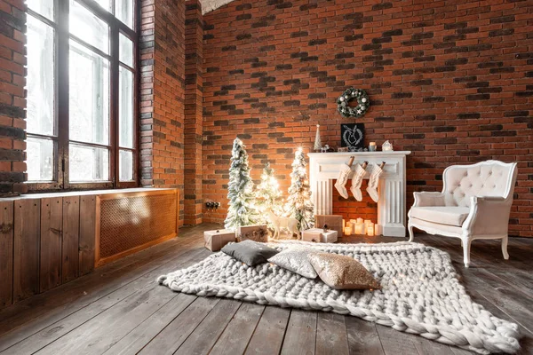 Apartamentos Loft, parede de tijolos com velas e grinalda de árvores de Natal. Meias de lã branca para o Pai Natal na lareira. Tapete de malha e cadeira, árvore de Natal — Fotografia de Stock