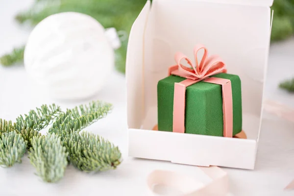 Mini postre de masa mousse cubierto de terciopelo verde. Envuelto individualmente en una caja blanca. Las ramas de abeto sobre fondo bokeh. Pastel europeo moderno. Cocina francesa. Caja de regalo —  Fotos de Stock