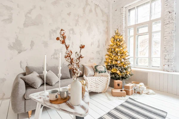 Light living room with Christmas tree. Comfortable sofa, high large Windows. Light white brick wall.