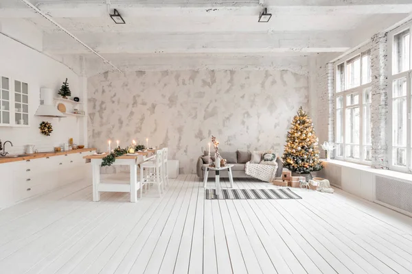 Loft stil lägenhet, stort rymligt vardagsrum med matbord och kök. Rum med julgran. Bekväm soffa, hög stora fönster. Ljus vit tegelvägg. — Stockfoto