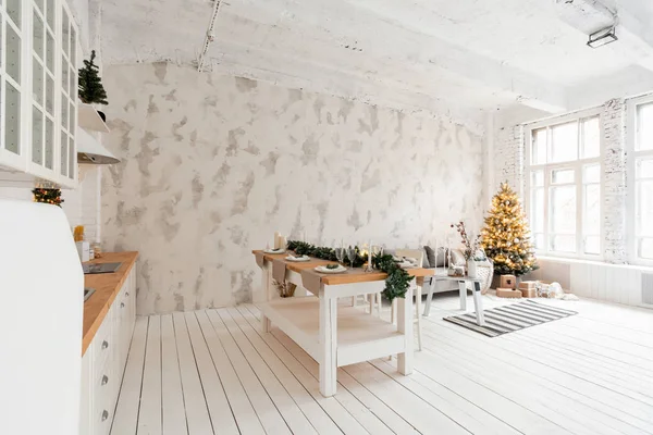 Loft stil lägenhet, stort rymligt vardagsrum med matbord och kök. Rum med julgran. Bekväm soffa, hög stora fönster. Ljus vit tegelvägg. — Stockfoto