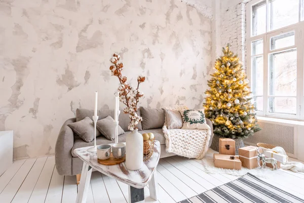 Salón luminoso con árbol de Navidad. Cómodo sofá, grandes ventanales. pared de ladrillo blanco claro . — Foto de Stock