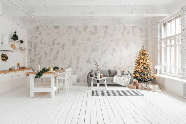Loft stil lägenhet, stort rymligt vardagsrum med matbord och kök. Rum med julgran. Bekväm soffa, hög stora fönster. Ljus vit tegelvägg. — Stockfoto