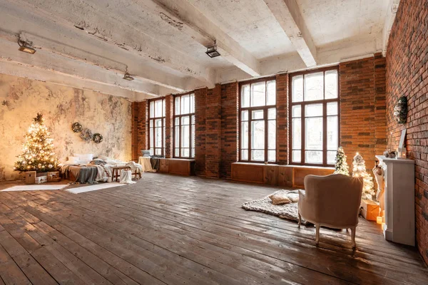 Loft stil lägenheter. Säng i sovrummet, hög stora fönster. Tegelvägg med ljus och julgran. varm och brun färg — Stockfoto