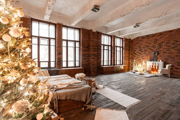 Loft apartamentos, pared de ladrillo con velas y corona de árboles de Navidad. Calcetines de lana blanca para Santa en la chimenea. Alfombra y silla de punto, árbol de Navidad — Foto de Stock