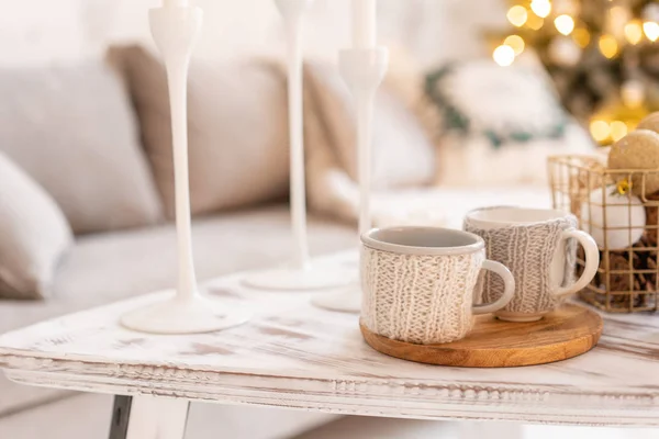 Gestrickte Wollbecher auf einem Holztisch. zwei Tassen heißen Kaffee. das Konzept der Wärme. Feiertage und Veranstaltungen. Herbst und Winter, Freizeitkonzept. gemütlich, bequem, weich. — Stockfoto