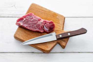 Çiğ et. Ham taze Dana biftek bir tahta Ahşap kesme ve oyma bıçağı. Beyaz ahşap arka plan, üstten görünüm, kopya alanı, gün ışığından yararlanma