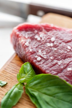 Çiğ et Marine tuz, biber ve fesleğen yaprak baharat ile. Sabah mutfakta. Ağaç kesme tahtası ham taze Dana biftek. Beyaz ahşap arka plan, üstten görünüm, kopya alanı, gün ışığından yararlanma