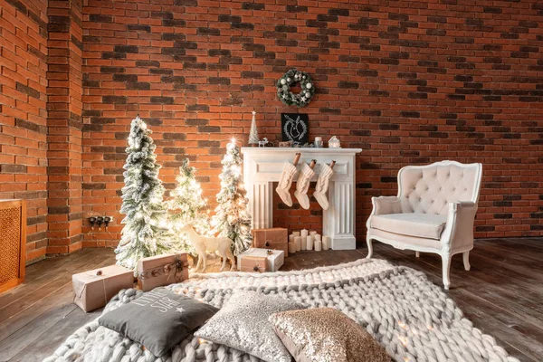 Loft apartamentos, pared de ladrillo con velas y corona de árboles de Navidad. Calcetines de lana blanca para Santa en la chimenea. Alfombra y silla de punto, árbol de Navidad — Foto de Stock
