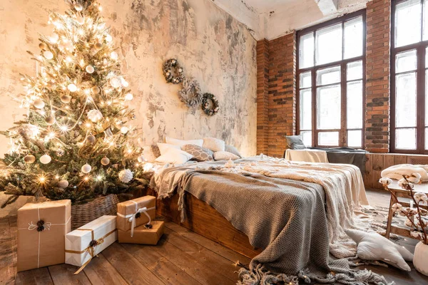Loft stil lägenheter. Säng i sovrummet, hög stora fönster. Tegelvägg med ljus och julgran. varm och brun färg — Stockfoto