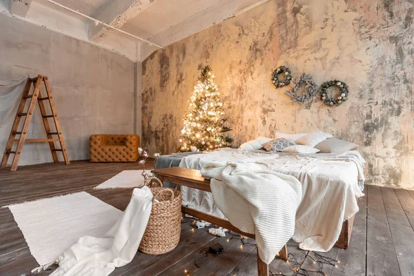 Wohnungen im Loft-Stil. Bett im Schlafzimmer, hohe große Fenster. Ziegelwand mit Kerzen und Weihnachtsbaum. warme und braune Farbe — Stockfoto