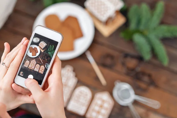 La chica hace una foto de Flatley para las redes sociales, el resultado de su trabajo. Blogging, blogger. Un montón de galletas de jengibre. Humor navideño, mañana de invierno. Ramas y formas de abeto para hornear . — Foto de Stock