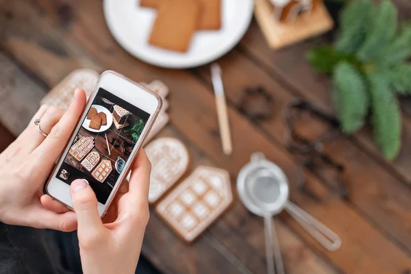 La chica hace una foto de Flatley para las redes sociales, el resultado de su trabajo. Blogging, blogger. Un montón de galletas de jengibre. Humor navideño, mañana de invierno. Ramas y formas de abeto para hornear . — Foto de Stock