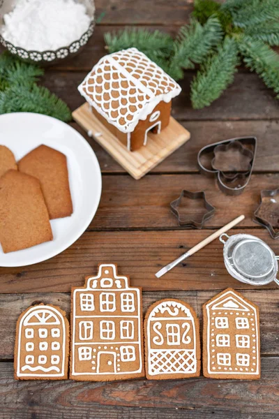 A lot of ginger biscuits in the form of European houses on brown wooden table. Decorated with white sweet glaze. Christmas mood, winter morning.