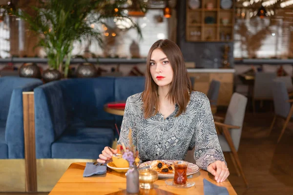 A young woman has Breakfast in a cafe. Oatmeal with salted caramel and prunes, in the original serving. Breakfast, pleasant morning, the beginning of the working day. looking into the camera — Stock Photo, Image