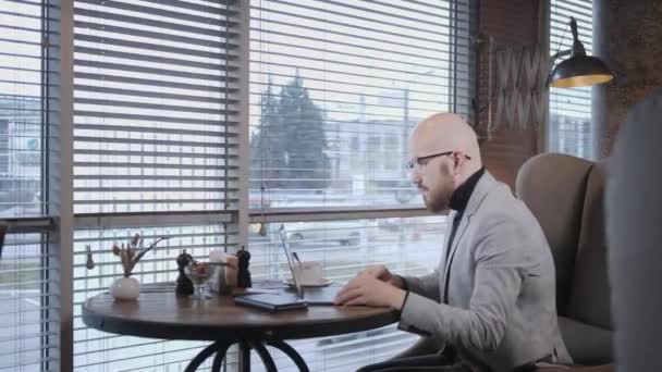 Porträt eines jungen Mannes mit Bart, der einen Anzug mit Brille trägt und auf den Monitor-Laptop blickt. erfolgreiche Menschen, Geschäftsmann in gemütlichem Café. Textlesen während der Arbeit am Netbook — Stockvideo