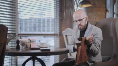 Sakallı genç adam portresi, bir takım elbise gözlüklü laptop deri çantaya koyar. Başarılı insanlar, işadamı rahat kafede. Netbook üzerinde çalışması sırasında metin okuma