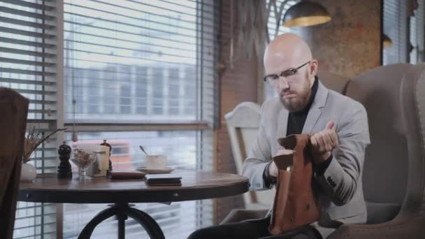 Portrait de jeune homme barbu, portant un costume dans les lunettes Met l'ordinateur portable dans un sac en cuir. Des gens qui réussissent, un homme d'affaires dans un café confortable. Lecture de texte pendant le travail sur netbook — Video