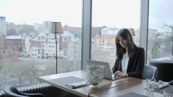 Junge Frau sitzt im Café am Holztisch. Auf dem Tisch liegt ein grauer Aluminium-Laptop. Mädchen bloggen, im Internet surfen, chatten — Stockvideo