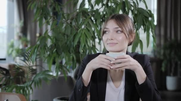 Junge Frau, die duftenden Kaffee trinkt. weiblicher Haltebecher vorhanden. Mädchen sitzt im Café am Holztisch. große Fenster, Blick auf die Stadt — Stockvideo