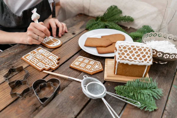Blank biscuit gingerbread, ready to decorate. Icing of Christmas bakery. Woman decorating honey gingerbread cookies on wooden brown table. closeup.