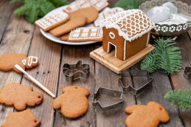 Sevimli küçük ev. Bir sürü farklı formunda kahverengi ahşap masa, zencefilli bisküvi. Beyaz tatlı sır ile dekore edilmiştir. Noel ruh hali, kış sabahı. Çam dalları