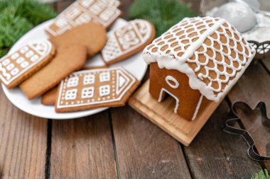 Sevimli küçük ev. Bir sürü farklı formunda kahverengi ahşap masa, zencefilli bisküvi. Beyaz tatlı sır ile dekore edilmiştir. Noel ruh hali, kış sabahı. Çam dalları