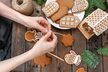 Genç bir kız kış sabahı kardan adam Noel şeklinde zencefilli kurabiye süsle. Kadın bal gingerbread çerezleri üzerinde buzlanma çizer. Ahşap kahverengi masa. kopya alanı.
