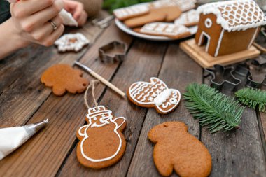 Genç bir kız yıldız Noel kış sabahı şeklinde zencefilli kurabiye süsle. Kadın bal gingerbread çerezleri üzerinde buzlanma çizer. Ahşap kahverengi masa. kopya alanı.