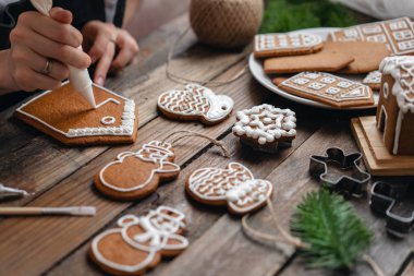 Genç bir kız kış sabahı zencefil çerezleri Noel süsler. Kadın buzlanma tatlım kurabiye evi üzerinde çizer. Ahşap kahverengi masa. kopya alanı. Boş Bisküvi Kurabiye evi, süslemek hazır.