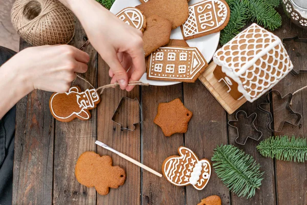 A young girl decorates ginger cookies in the form of snowman Christmas winter morning. Woman draws Icing on honey gingerbread cookies. Wooden brown table. copy space.
