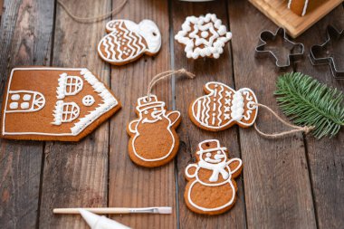 Genç bir kız kış sabahı zencefil çerezleri Noel süsler. Kadın buzlanma tatlım kurabiye evi üzerinde çizer. Ahşap kahverengi masa. kopya alanı. Boş Bisküvi Kurabiye evi, süslemek hazır.