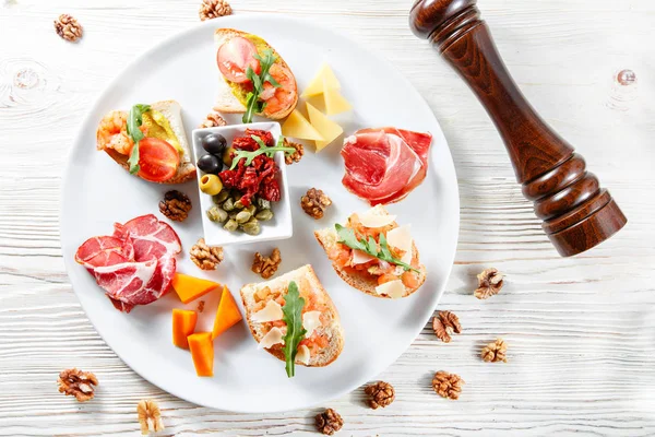 İtalyan meze plakalı. Bir kiraz domates Bruschetta ve karides. Parmesan peyniri, salam, yeşil kapari, zeytin, kurutulmuş domates ve ceviz. — Stok fotoğraf