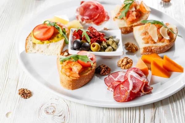 İtalyan meze plakalı. Bir kiraz domates Bruschetta ve karides. Parmesan peyniri, salam, yeşil kapari, zeytin, kurutulmuş domates ve ceviz. — Stok fotoğraf