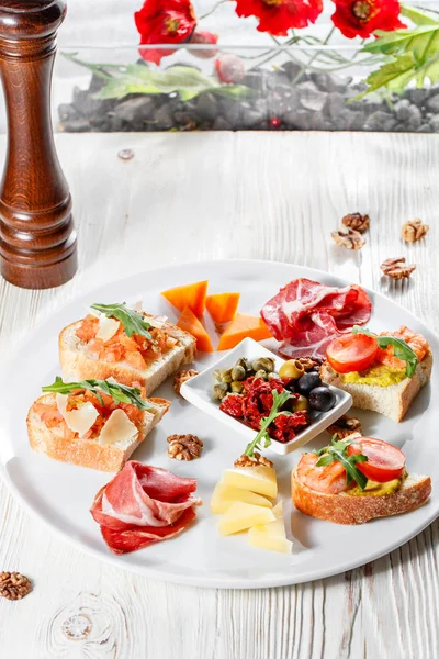 İtalyan meze plakalı. Bir kiraz domates Bruschetta ve karides. Parmesan peyniri, salam, yeşil kapari, zeytin, kurutulmuş domates ve ceviz. — Stok fotoğraf