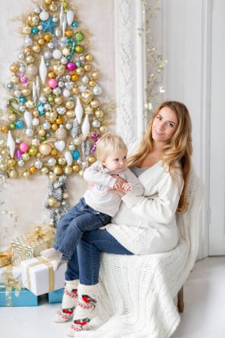 Anne çocukla çalış. Mutlu aile portresi olarak ana sayfa - genç hamile anne küçük oğlunu kucaklar. Yeni Yılınız Kutlu Olsun. süslü Noel ağacı. Noel sabahı parlak oturma odasında.