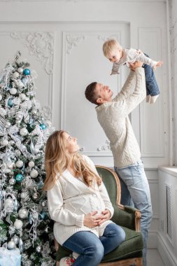Genç Anne aptal ve küçük oğlu ile oynamak. Mutlu bir aile evde eğleniyor. Noel sabahı parlak oturma odasında. Baba, hamile anne ve bebek oğulları. Yeni Yılınız Kutlu Olsun.