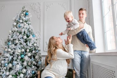 Genç Anne aptal ve küçük oğlu ile oynamak. Mutlu bir aile evde eğleniyor. Noel sabahı parlak oturma odasında. Baba, hamile anne ve bebek oğulları. Yeni Yılınız Kutlu Olsun.