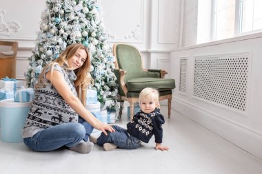 Anne çocukla çalış. Katta oturan. Mutlu aile portresi olarak ana sayfa - genç hamile anne küçük oğlunu kucaklar. Yeni Yılınız Kutlu Olsun. Noel sabahı parlak oturma odasında.