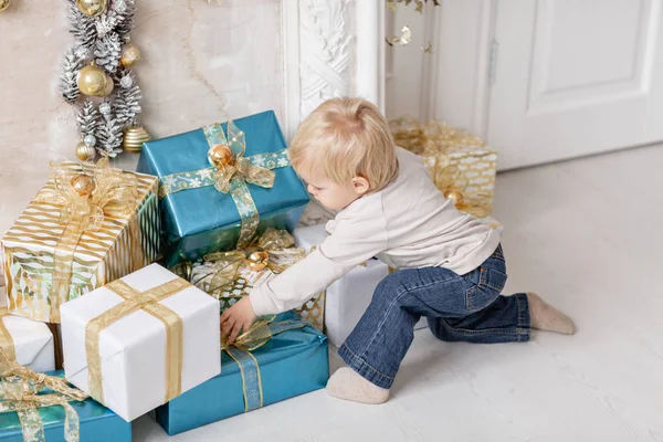 Un niño pequeño cerca de muchos regalos. Feliz año nuevo. árbol de Navidad decorado. Mañana de Navidad en salón luminoso —  Fotos de Stock