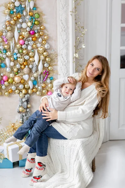 Anne çocukla çalış. Mutlu aile portresi olarak ana sayfa - genç hamile anne küçük oğlunu kucaklar. Yeni Yılınız Kutlu Olsun. süslü Noel ağacı. Noel sabahı parlak oturma odasında. — Stok fotoğraf