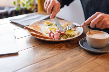 Adam yemek. Bıçak ve çatal elinde. Masaya servis kahvaltı... Amerikan tarzı kahvaltı kızarmış yumurta, sosis, yeşil bezelye ve tost ile. Sağlıklı bir sabah kavramı.