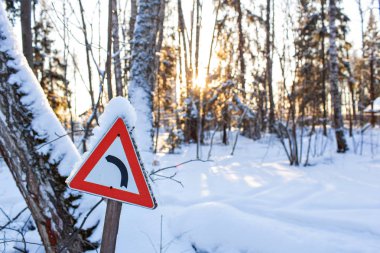 Kar, arka planda şafak güneş ile pul sol hareketle gösteren kırmızı üçgen yol trafik işaret. Noel soğuk sabah. Kış manzarası, sakin doğa güneş ışığı altında Park