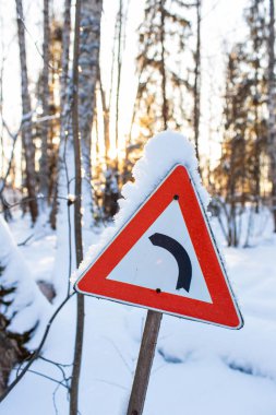Kar, arka planda şafak güneş ile pul sol hareketle gösteren kırmızı üçgen yol trafik işaret. Noel soğuk sabah. Kış manzarası, sakin doğa güneş ışığı altında Park