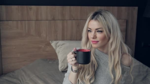 Hermosa mujer rubia sosteniendo taza de cerámica de té o café disfrutar. Hora del té en la cama. Mirando la ventana y bebiendo té. Buenos días. Una chica joven y bonita relajándose. Feliz concepto de invierno . — Vídeo de stock