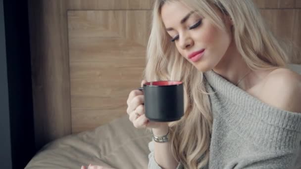 Hermosa mujer rubia sosteniendo taza de cerámica de té o café disfrutar. Hora del té en la cama. Mirando la ventana y bebiendo té. Buenos días. Una chica joven y bonita relajándose. Feliz concepto de invierno . — Vídeo de stock