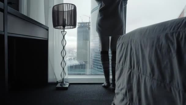 Widok na piękny blond kobieta stoi patrząc spośród pełnej długości okna luksus nowoczesny apartament lub Pokój korzystających zima rano i miasto drapaczy chmur Zobacz czuć się szczęśliwi z tyłu — Wideo stockowe